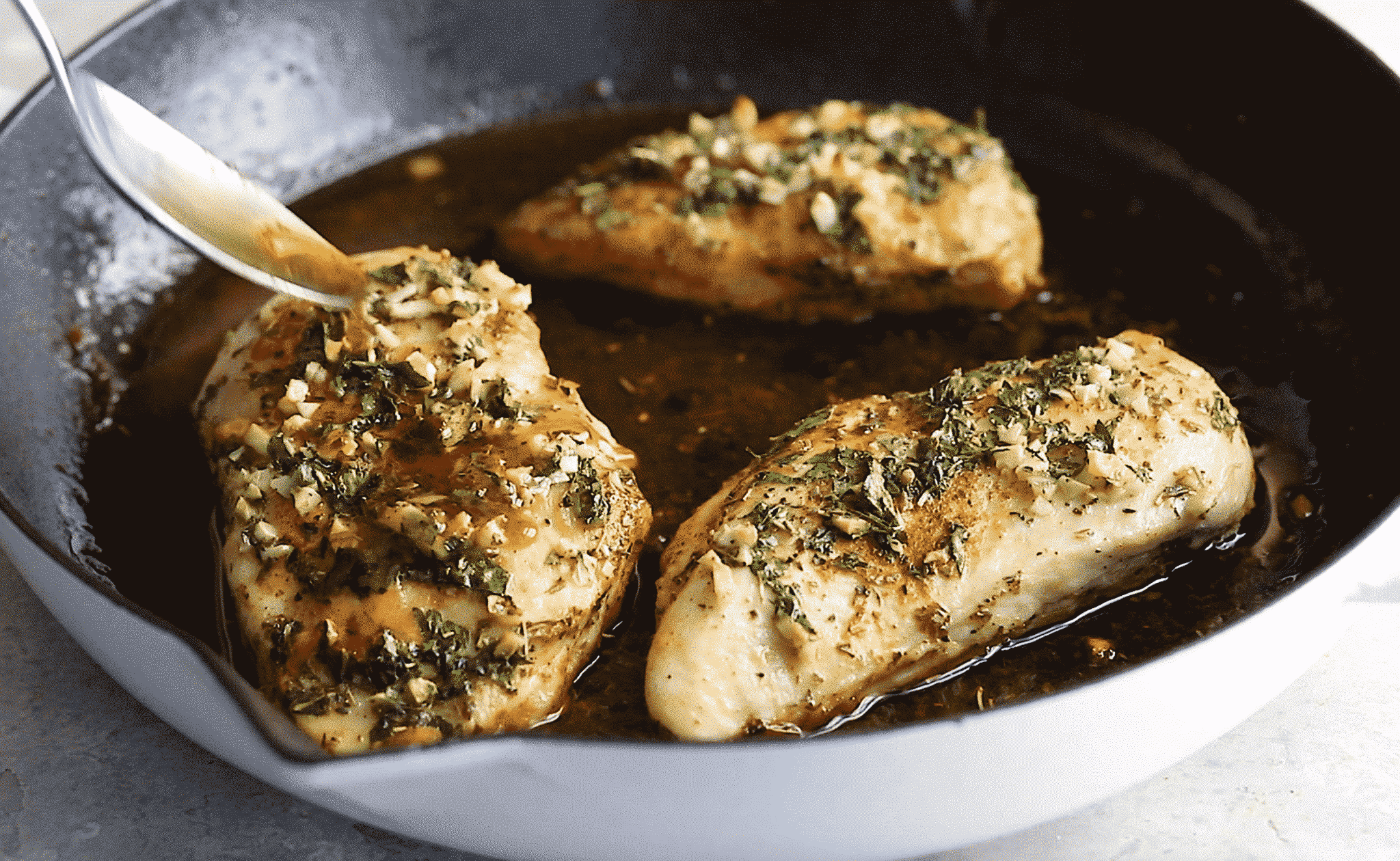 close up view of someone three chicken breast with garlic butter sauce in a cast iron skillet