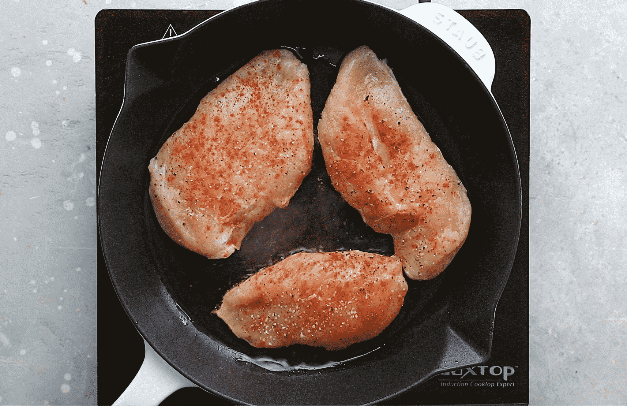 overhead view of a cast iron skillet containing raw chicken breast