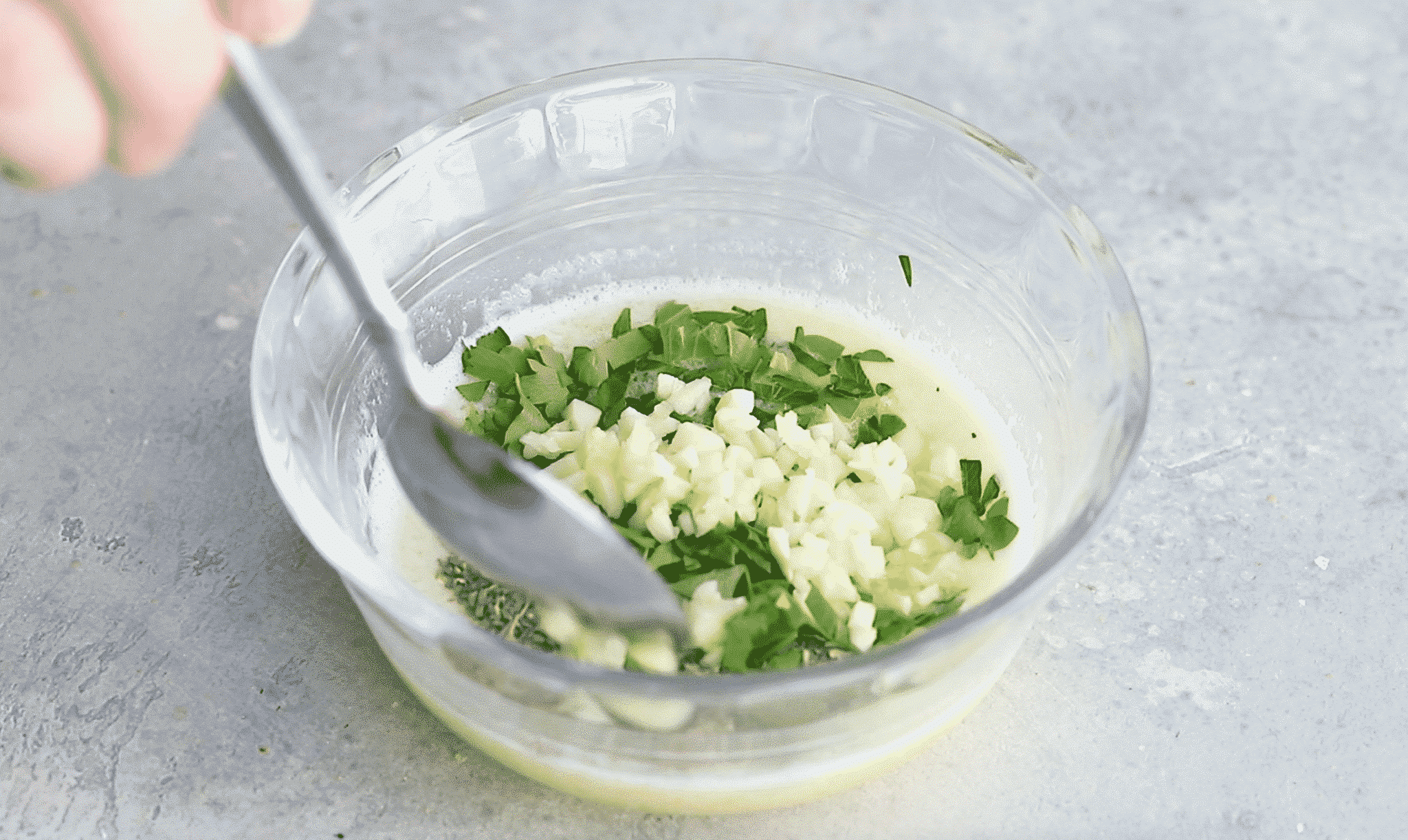 A small glass bowl of melted butter, garlic and parsley