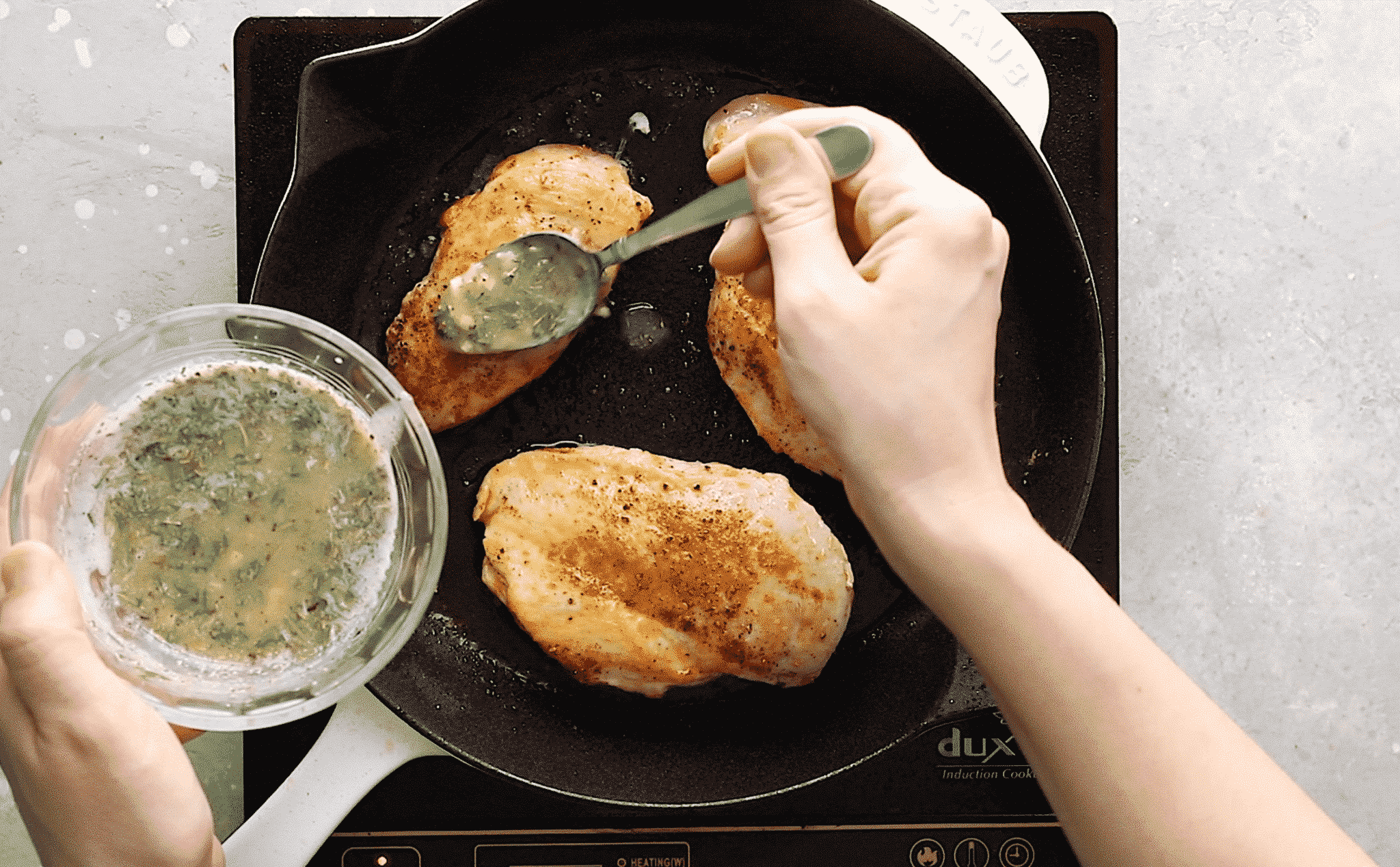 overhead view of someone pouring melted butter over two chicken breast in a cast iron skillet