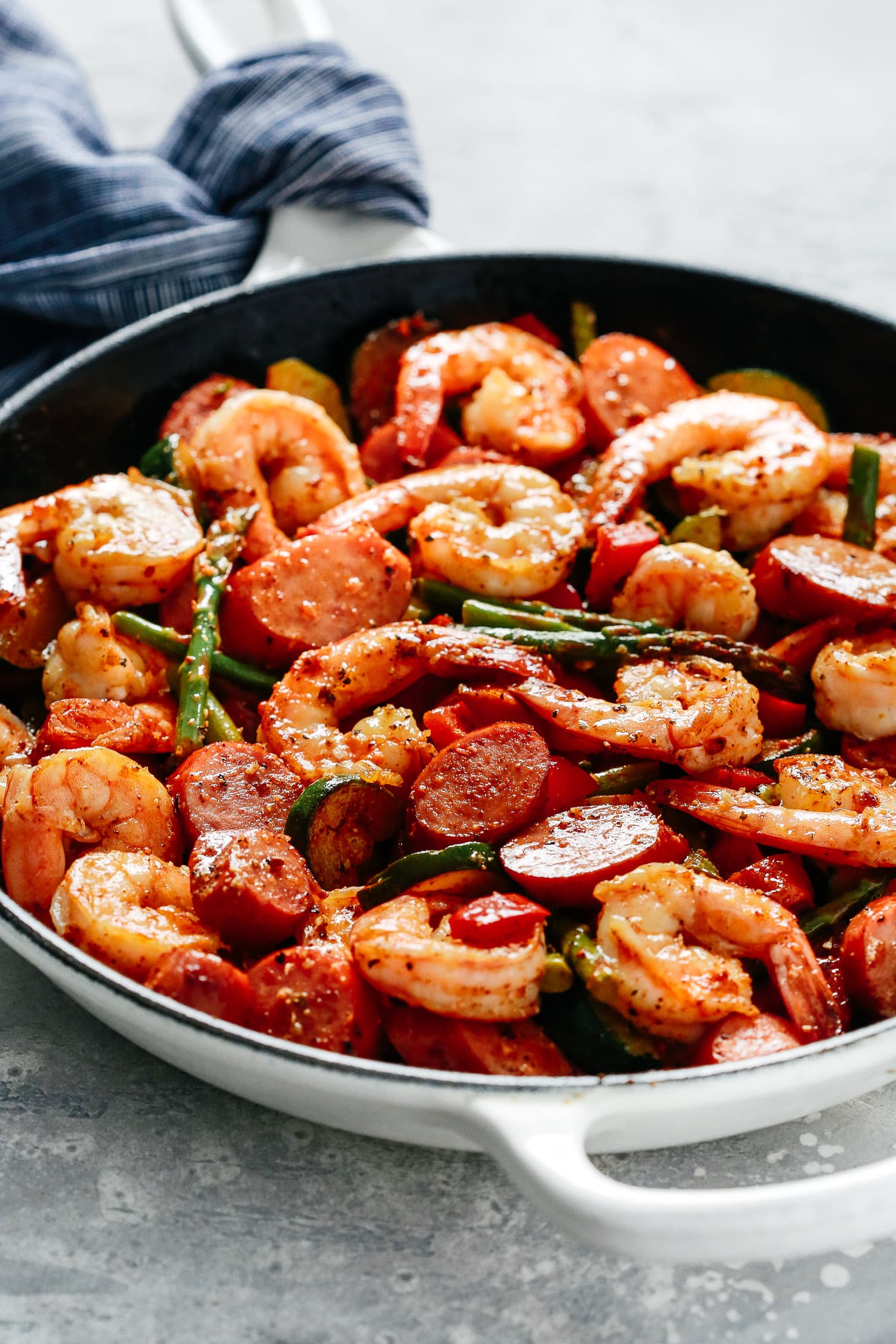 A white skillet with shrimp, sausage, and asparagus. 