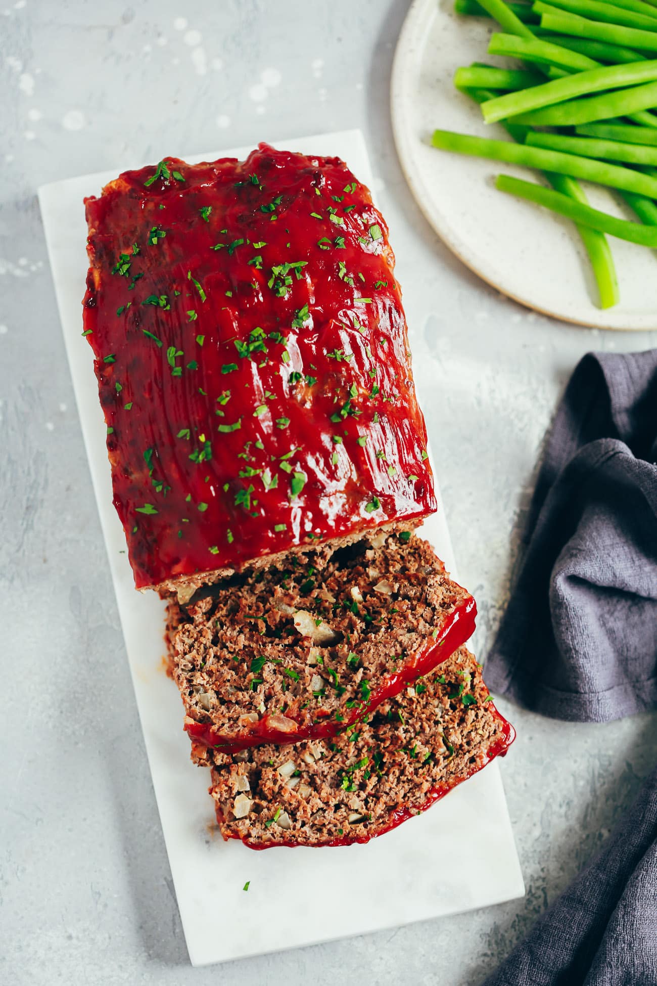 meatloaf on a cutting board next to green beans