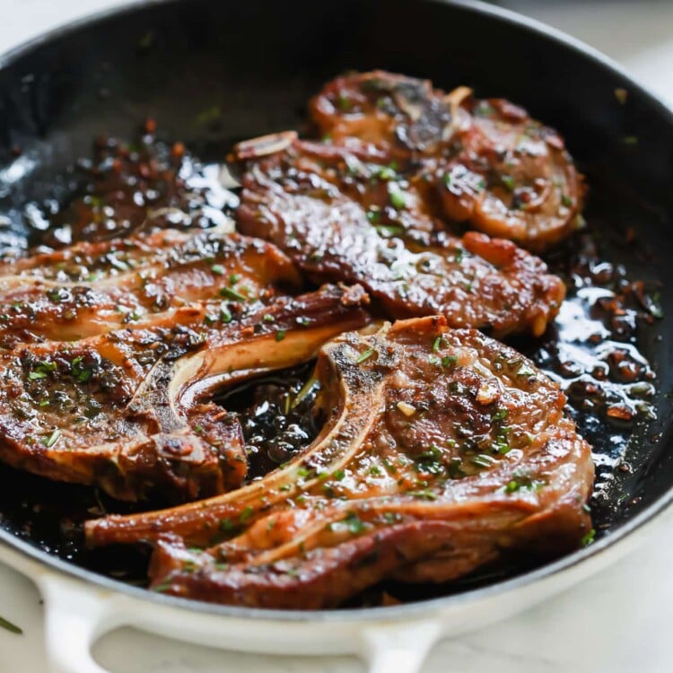 A close up of a white cast iron skillet containing Lamb Chops