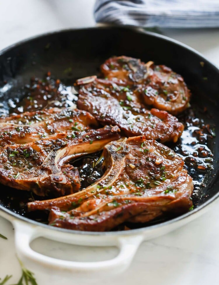 A close up of a white cast iron skillet containing Lamb Chops