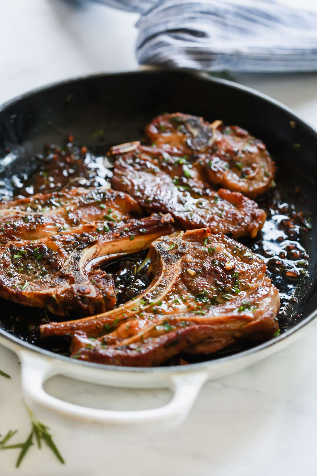 A close up of a white cast iron skillet containing Lamb Chops 