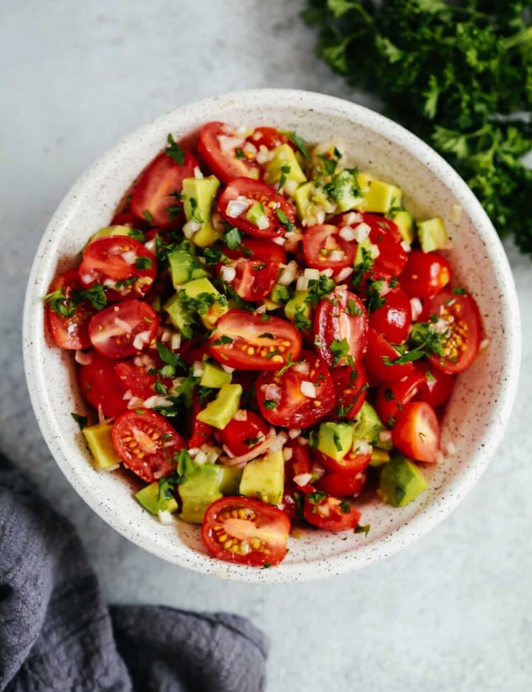 An overhead photo of an avocado tomato salad in a white bowl.
