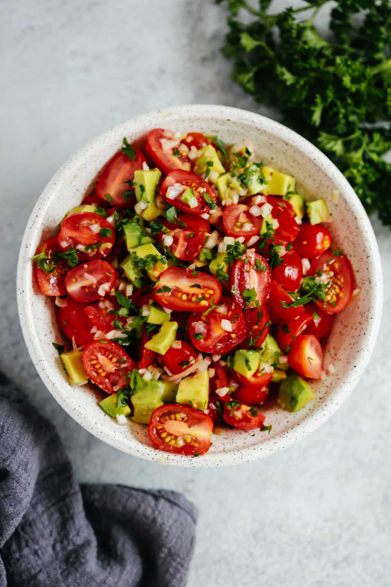 An overhead photo of an avocado tomato salad in a white bowl.