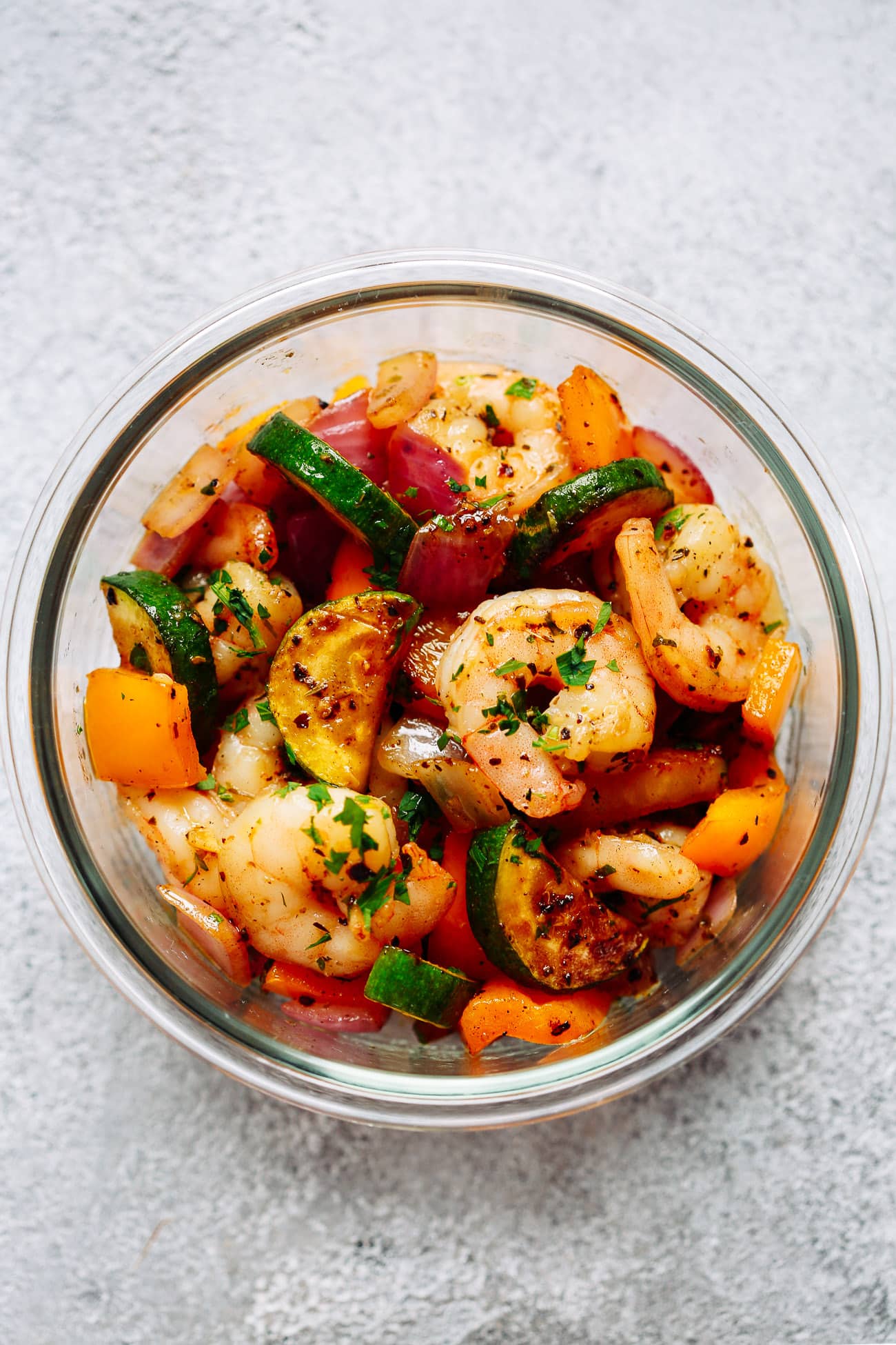 Garlic shrimp and veggies meal prep bowls - a make ahead freezer meal that will save you so much time in the kitchen! Succulent shrimp in garlic butter sauce with zucchini, bell peppers, and onion. This shrimp dinner will become your favorite easy meal prep recipe. close up of a glass bowl containing lots of vegetables and cooked shrimp