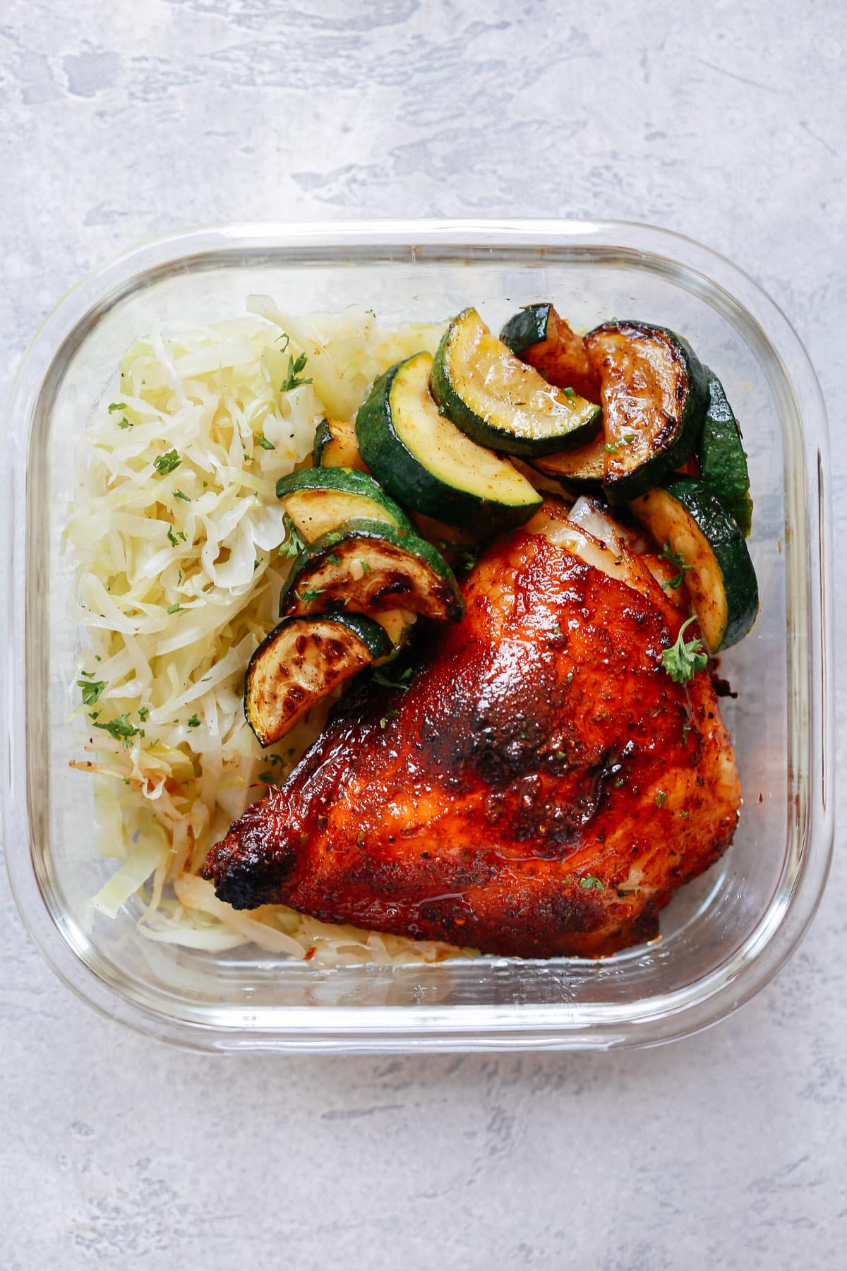Spicy Chicken with Sauteed Cabbage and Zucchini in glass meal prep container 