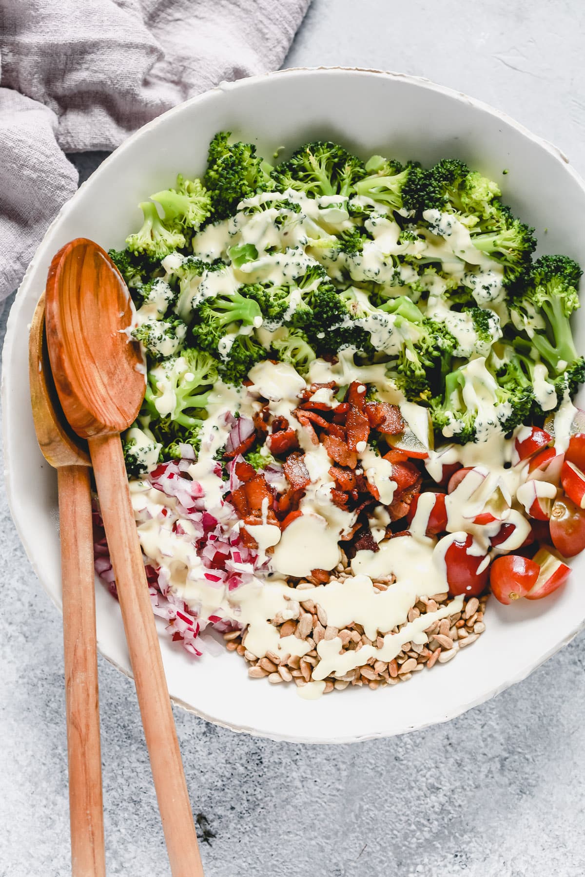 salad in white bowl with broccoli, tomatoes, bacon, onion, sesame seeds and dressing