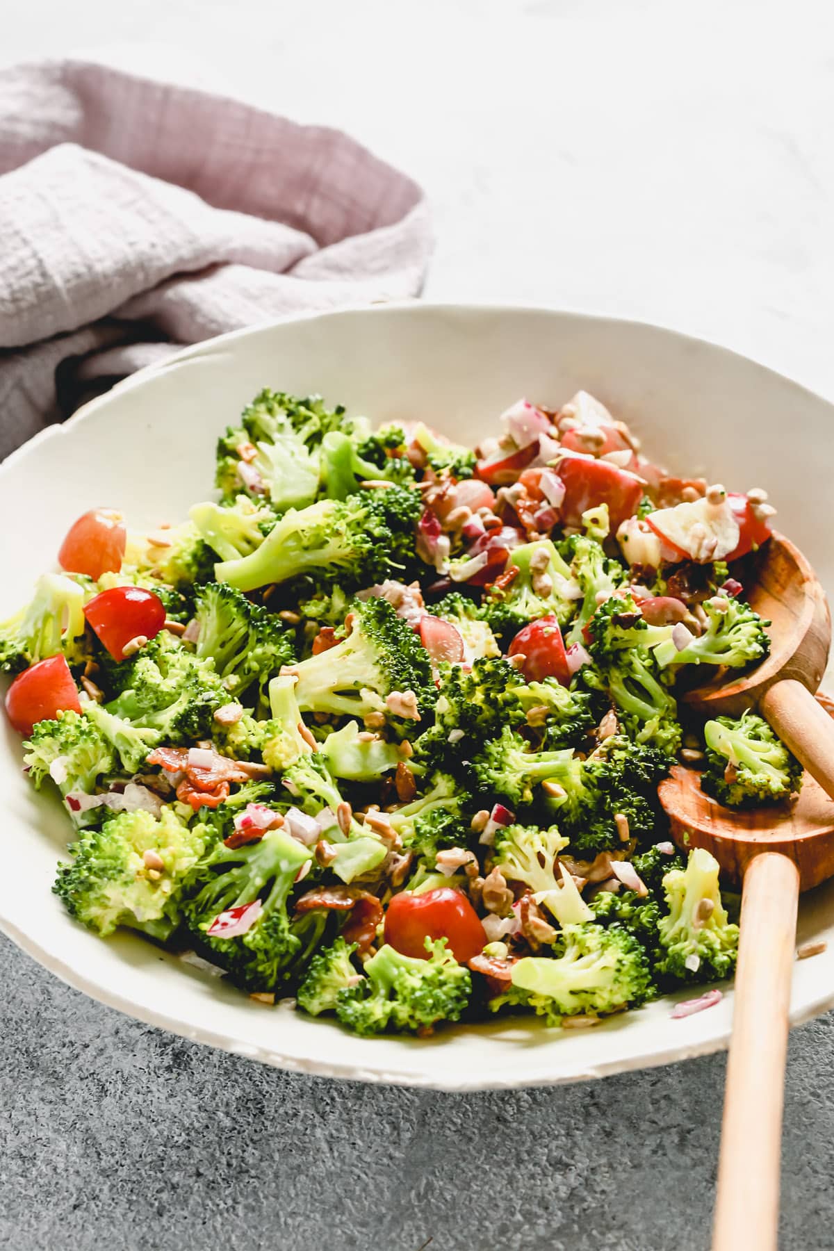 A white plate containing broccoli salad with two wooden spoons. 