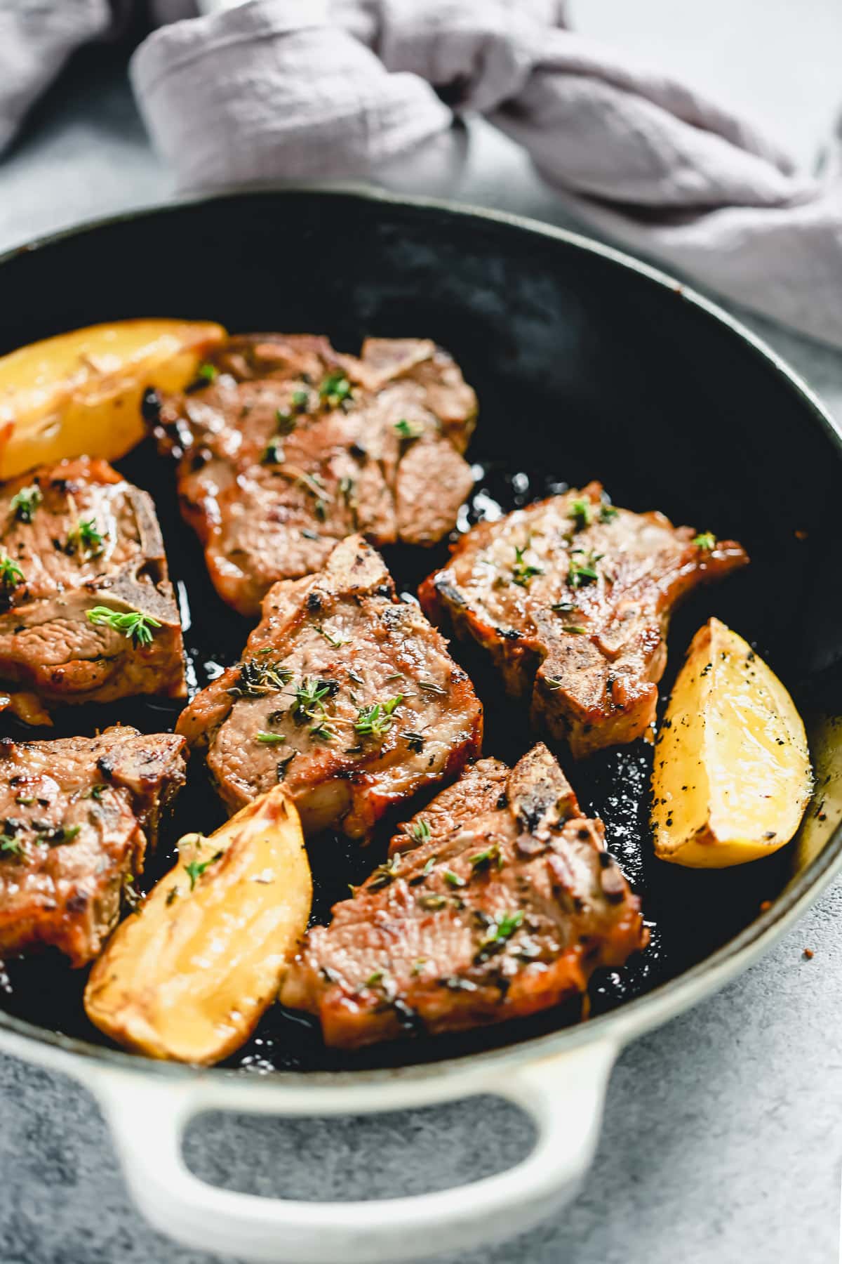 lamb chops cooking in pan with fresh lemon wedges and sprigs of thyme