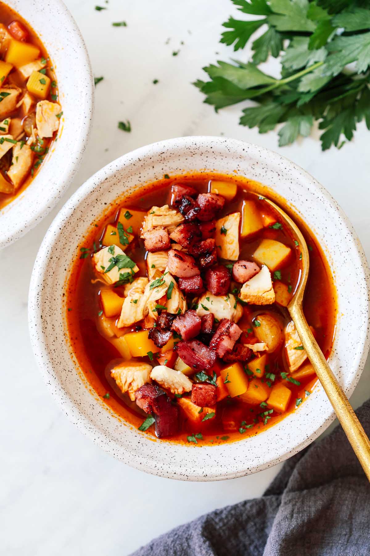 Turkey vegetable soup in a white bowl with a golden spoon inside.