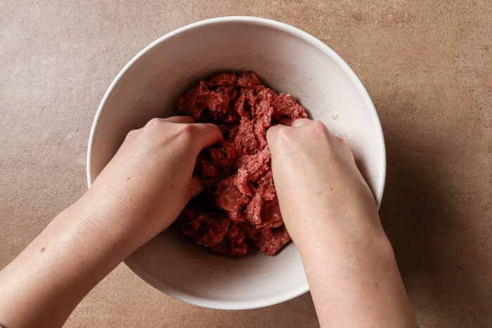 Hands mixing the ingredients to make the cocktail meatballs.