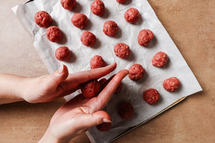 Hands rolling the mixture to form meatballs.