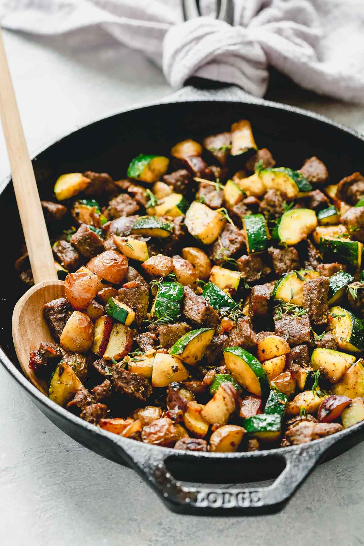 Beef and zucchini in a black cast iron with a spoon inside.