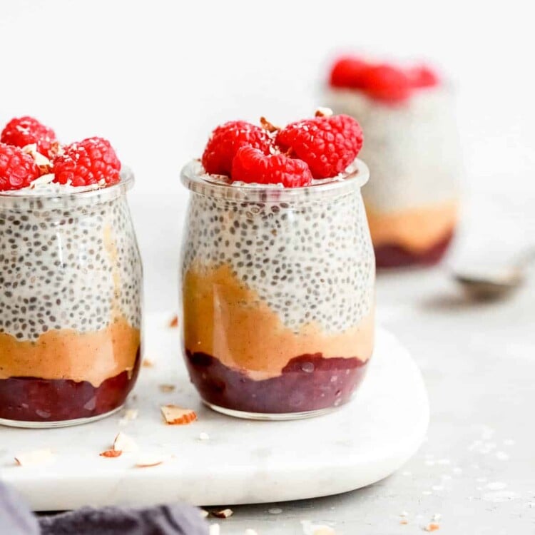 chia seed pudding topped with raspberries in small glass jars