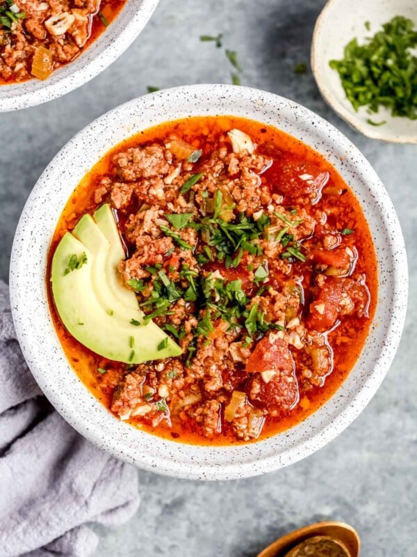 overhead view of a full white bowl of keto chili with avocado slices on top