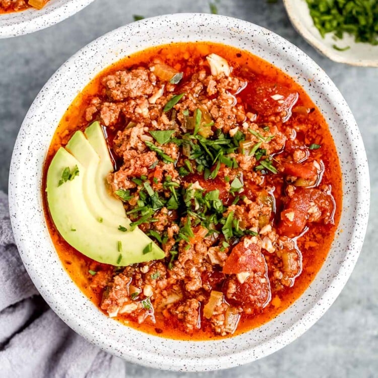 overhead view of a full white bowl of keto chili with avocado slices on top