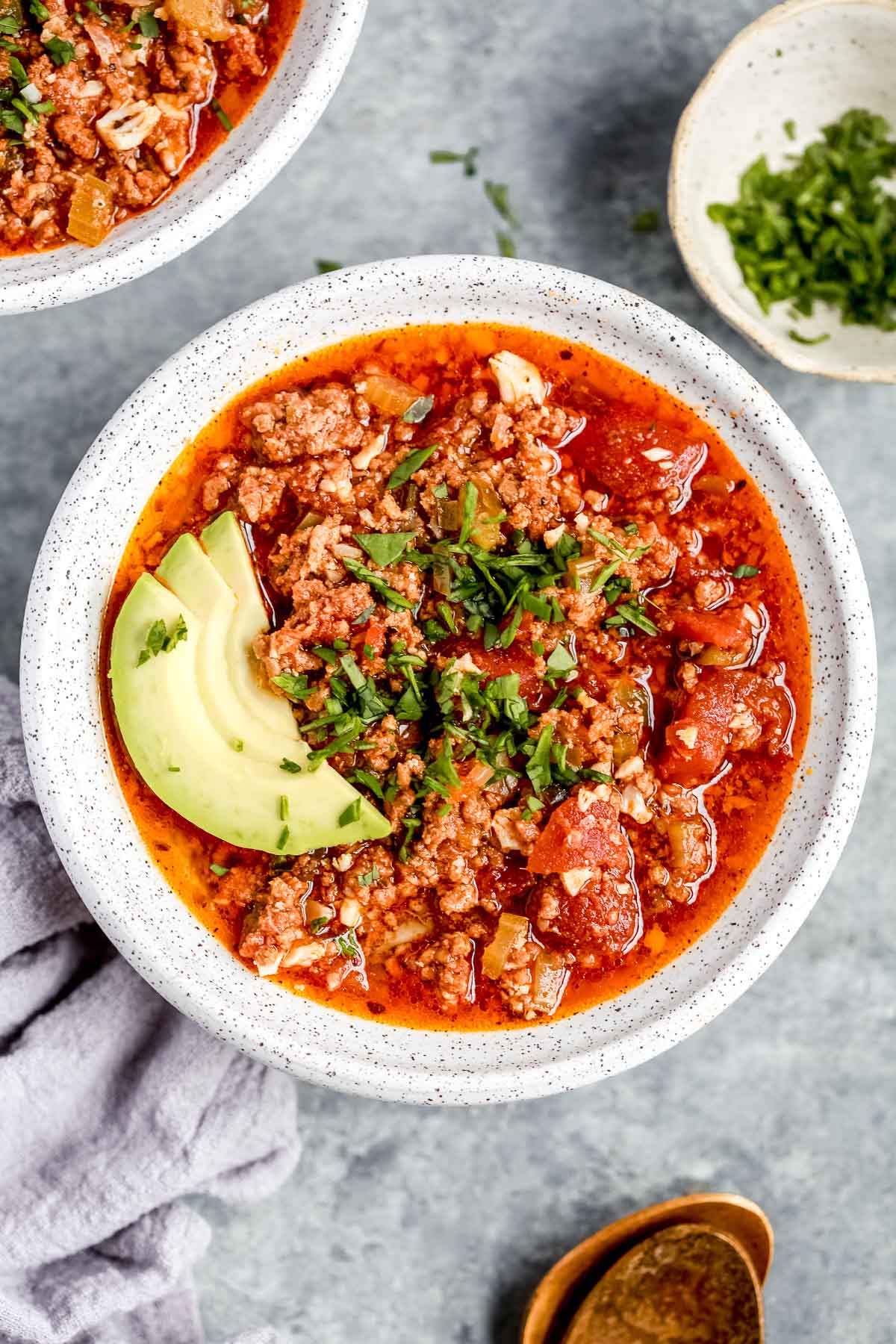 overhead view of a full white bowl of keto chili with avocado slices on top