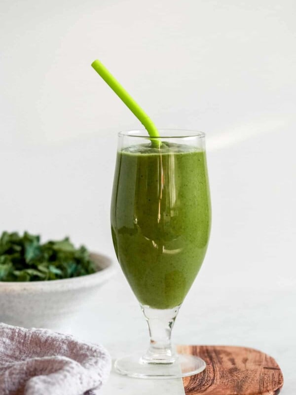 green keto smoothie in a tall glass with a straw