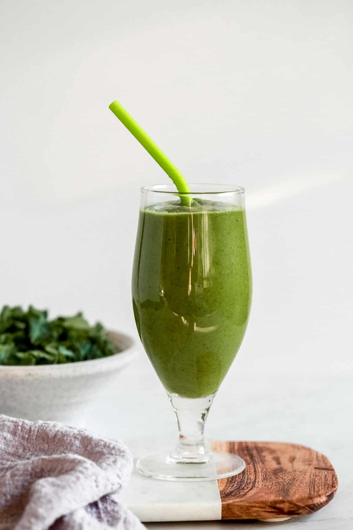 green keto smoothie in a tall glass with a straw 