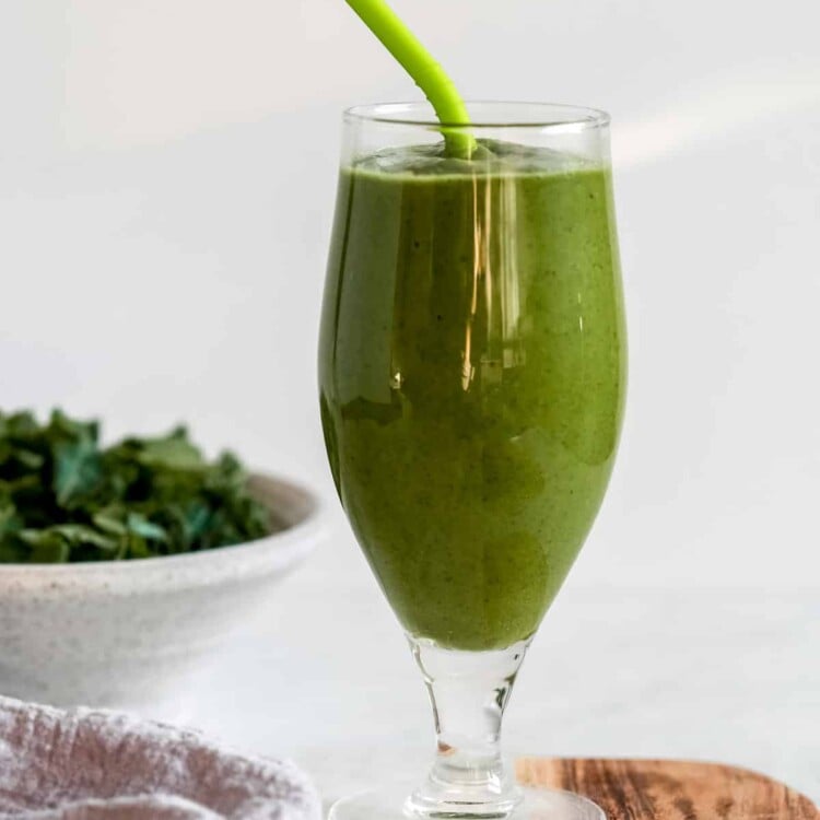 green keto smoothie in a tall glass with a straw