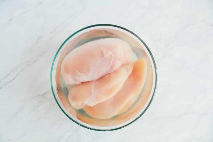 overhead view of a glass bowl containing water and raw chicken breast