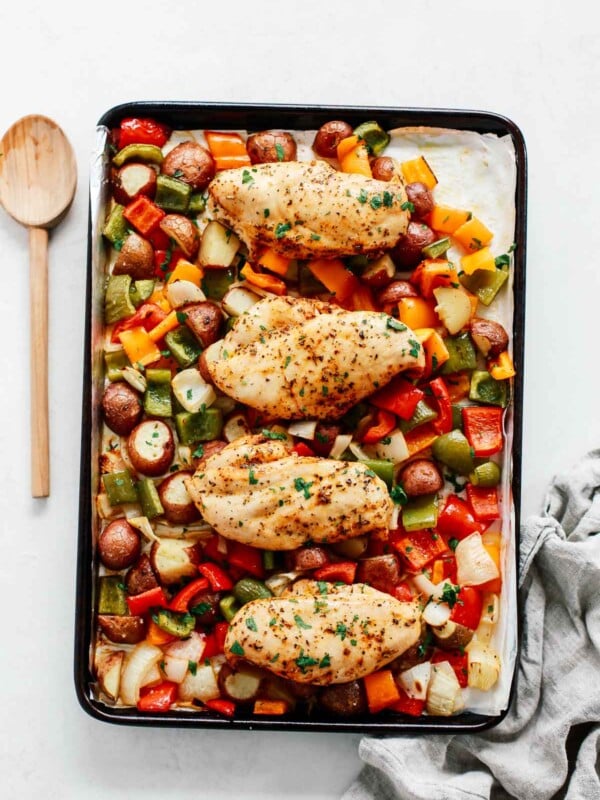 Sheet pan chicken with vegetables in a baking sheet with a spoon beside it.
