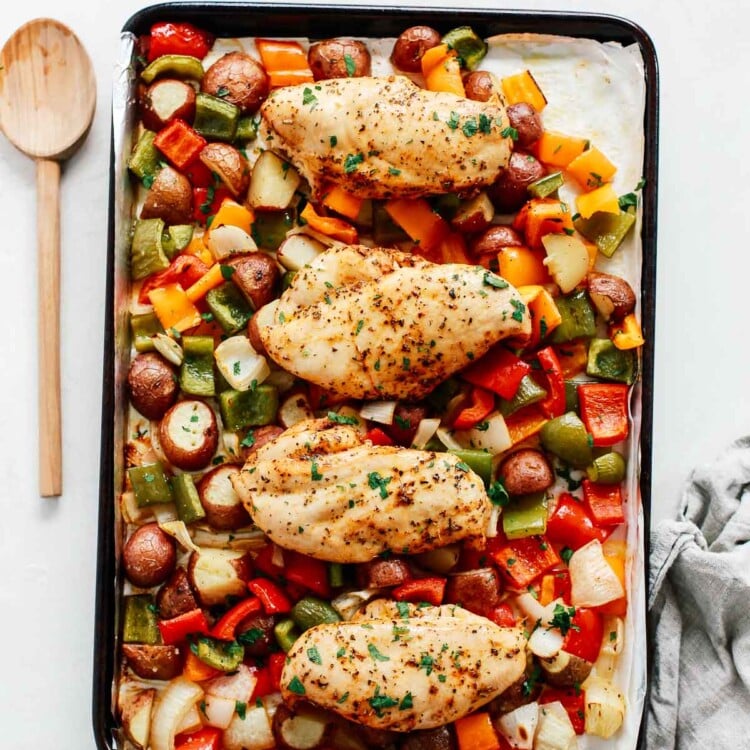 Sheet pan chicken with vegetables in a baking sheet with a spoon beside it.