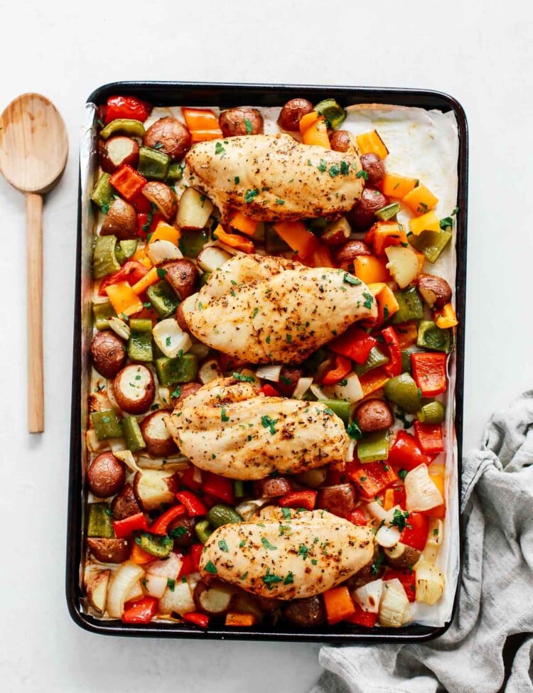 Sheet pan chicken with vegetables in a baking sheet with a spoon beside it.