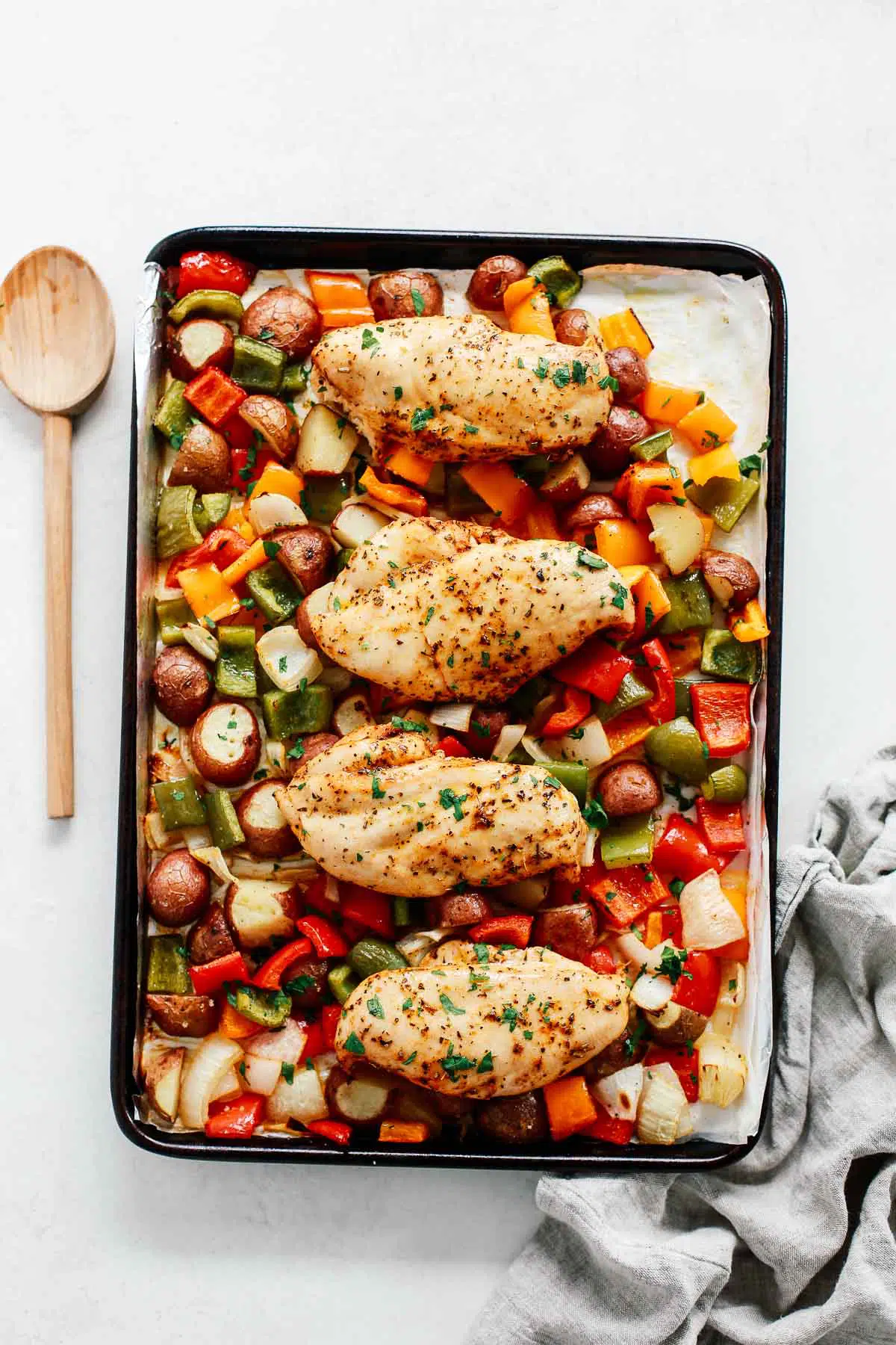 Sheet pan chicken with vegetables in a baking sheet with a spoon beside it.