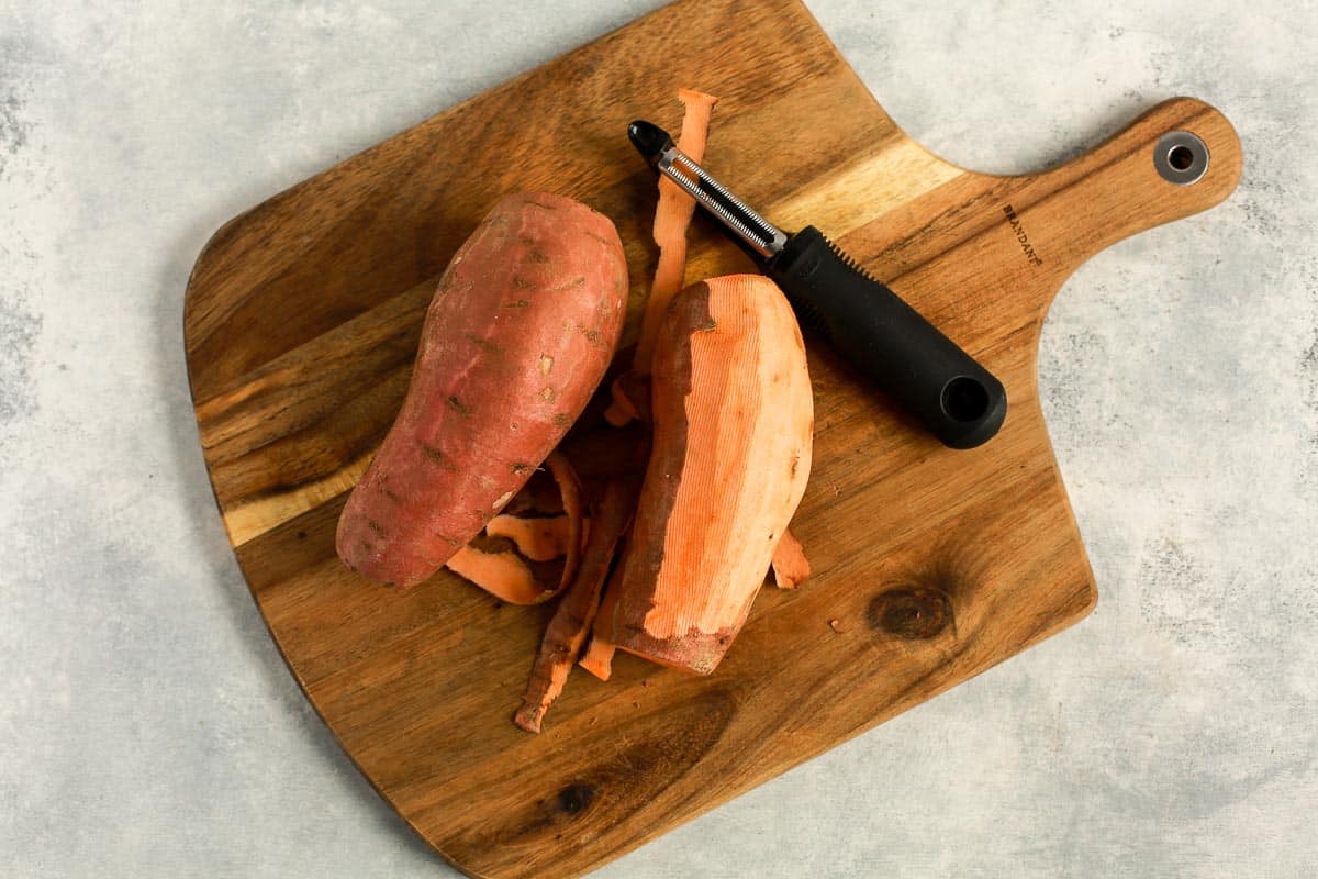 partial peeled sweet potato on a wooden board.