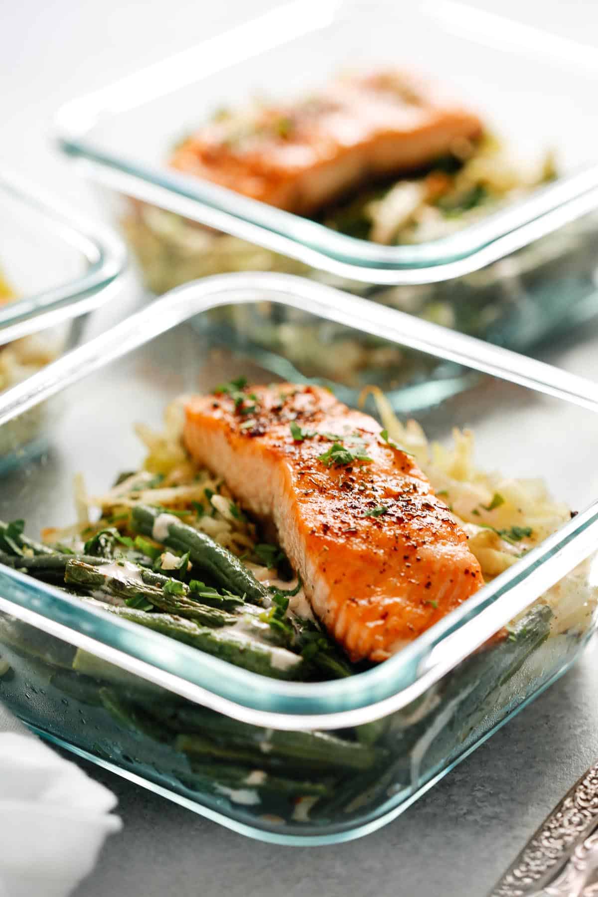 broiled salmon filet in square glass container with green beans and cabbage