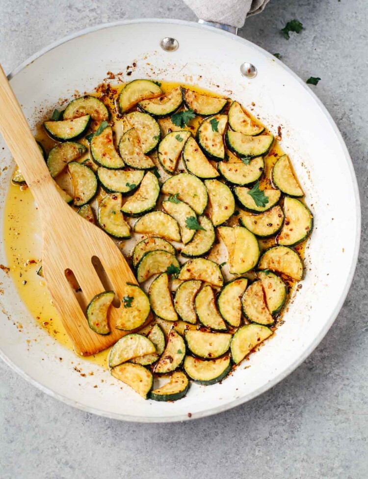 sautéed zucchini in a white bowl with wooden spoon