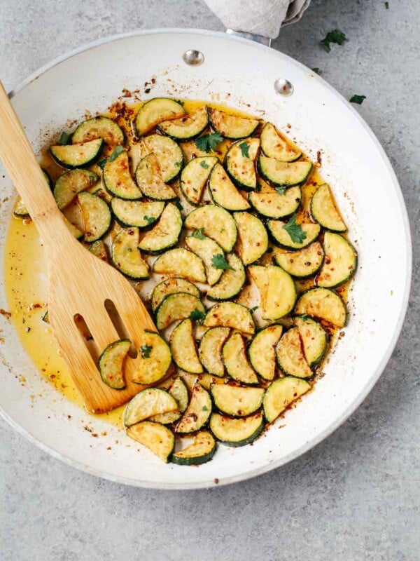 sautéed zucchini in a white bowl with wooden spoon