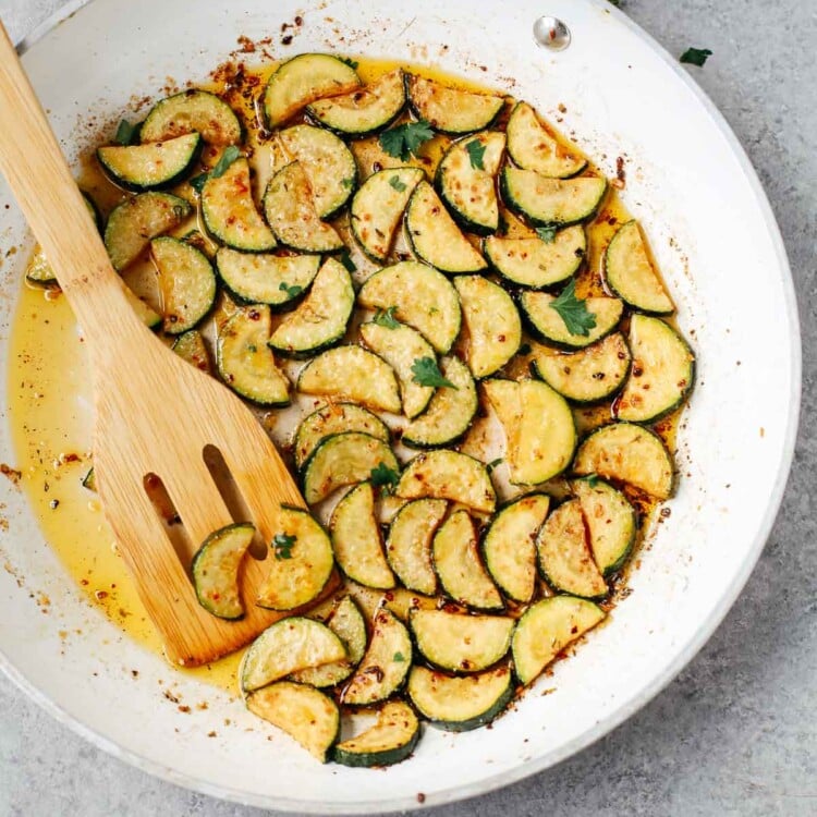 sautéed zucchini in a white bowl with wooden spoon