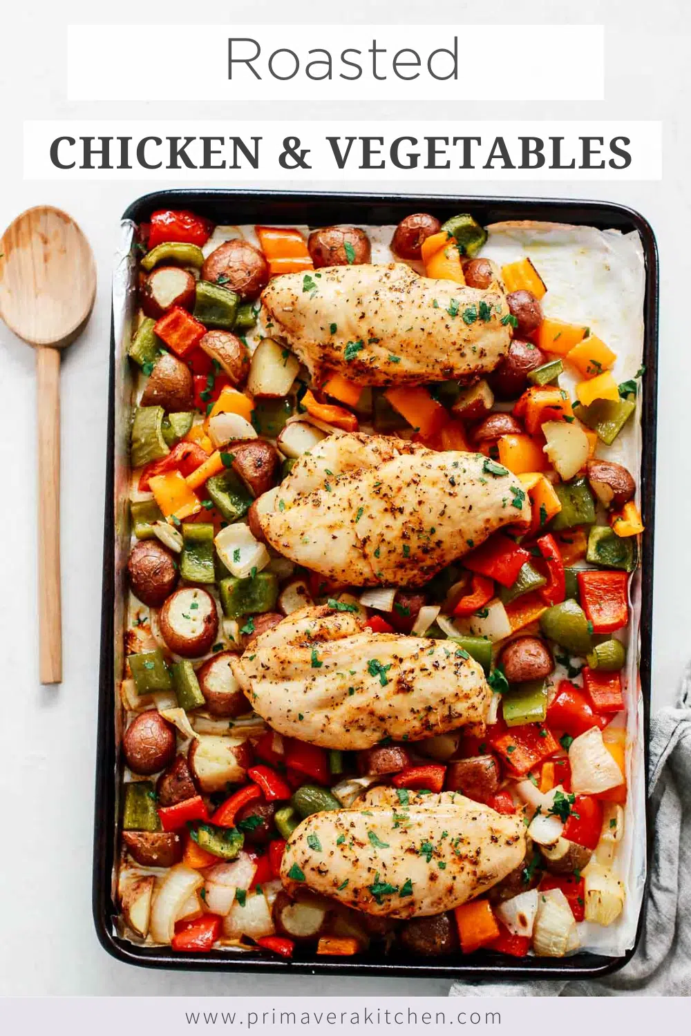 overhead view of roasted chicken and vegetables on a baking sheet with a wooden spoon on the side