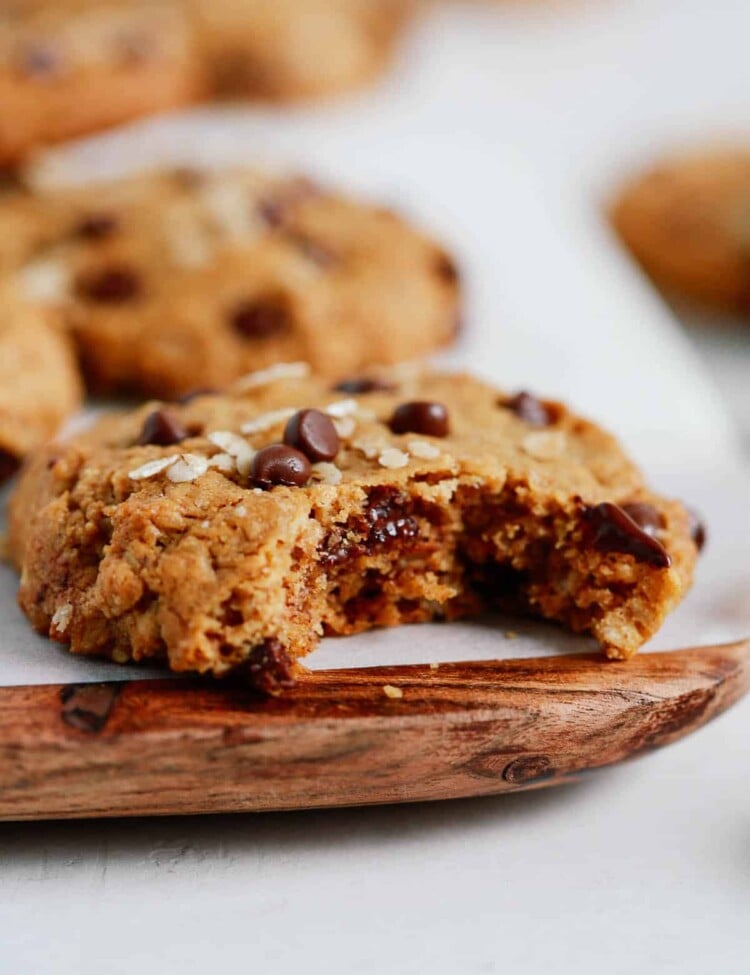Chocolate chip cookies with a bite taken out of it on a wooden serving board