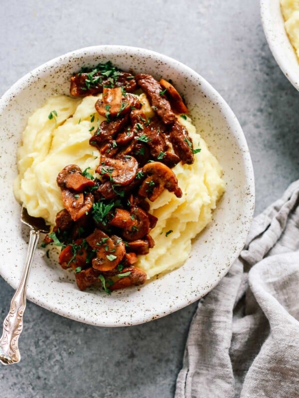 Bowl of mashed potatoes topped with steak and mushrooms