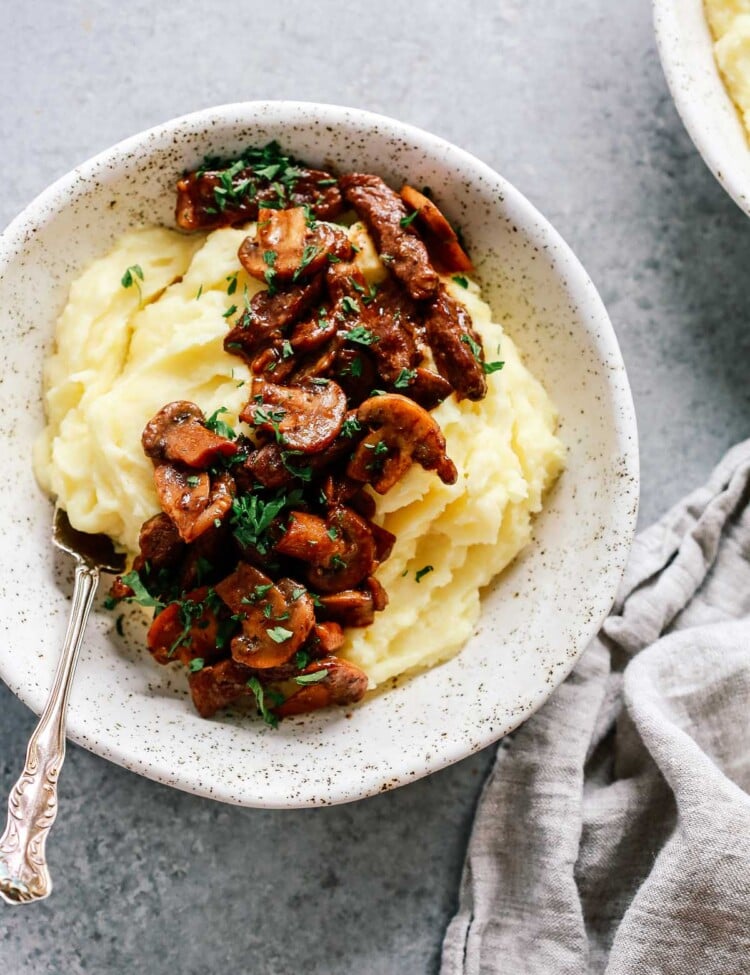 Bowl of mashed potatoes topped with steak and mushrooms