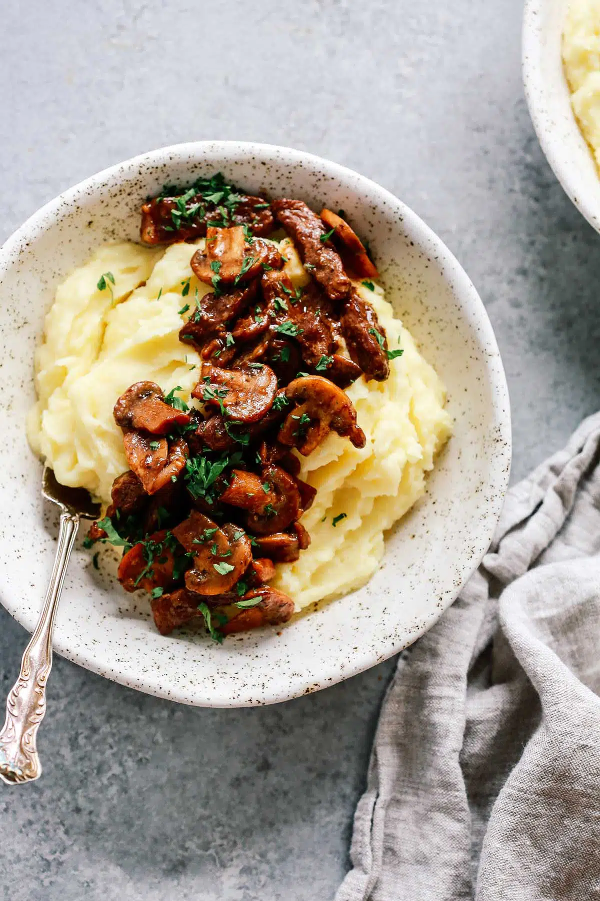 Bowl of mashed potatoes topped with steak and mushrooms