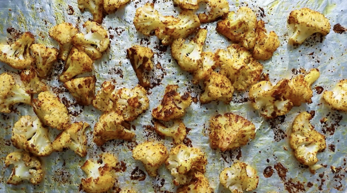 Roasted cauliflower florets, seasoned and slightly browned, are spread out on a silver baking sheet, showcasing a delicious Roasted Cauliflower Recipe.
