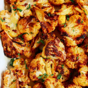 A close-up of Spicy Roasted Cauliflower florets coated in aromatic spices, garnished with chopped herbs, and served on a white rectangular dish. Text above reads Spicy Roasted Cauliflower Recipe.