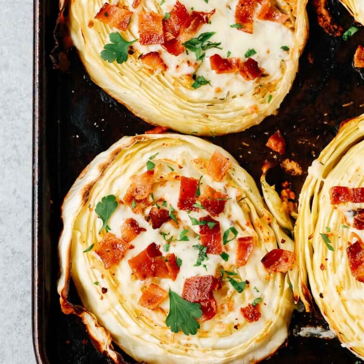 overhead view of roasted cabbage steaks with mozzarella and bacon on a baking sheet