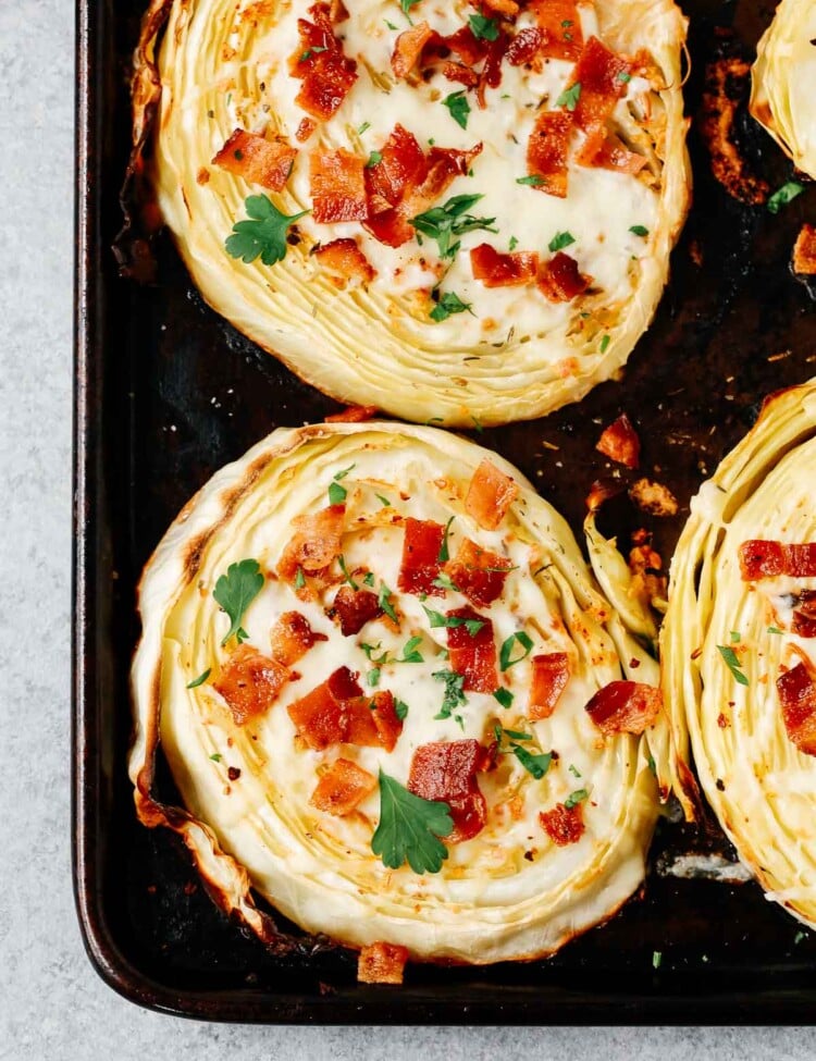 overhead view of roasted cabbage steaks with mozzarella and bacon on a baking sheet