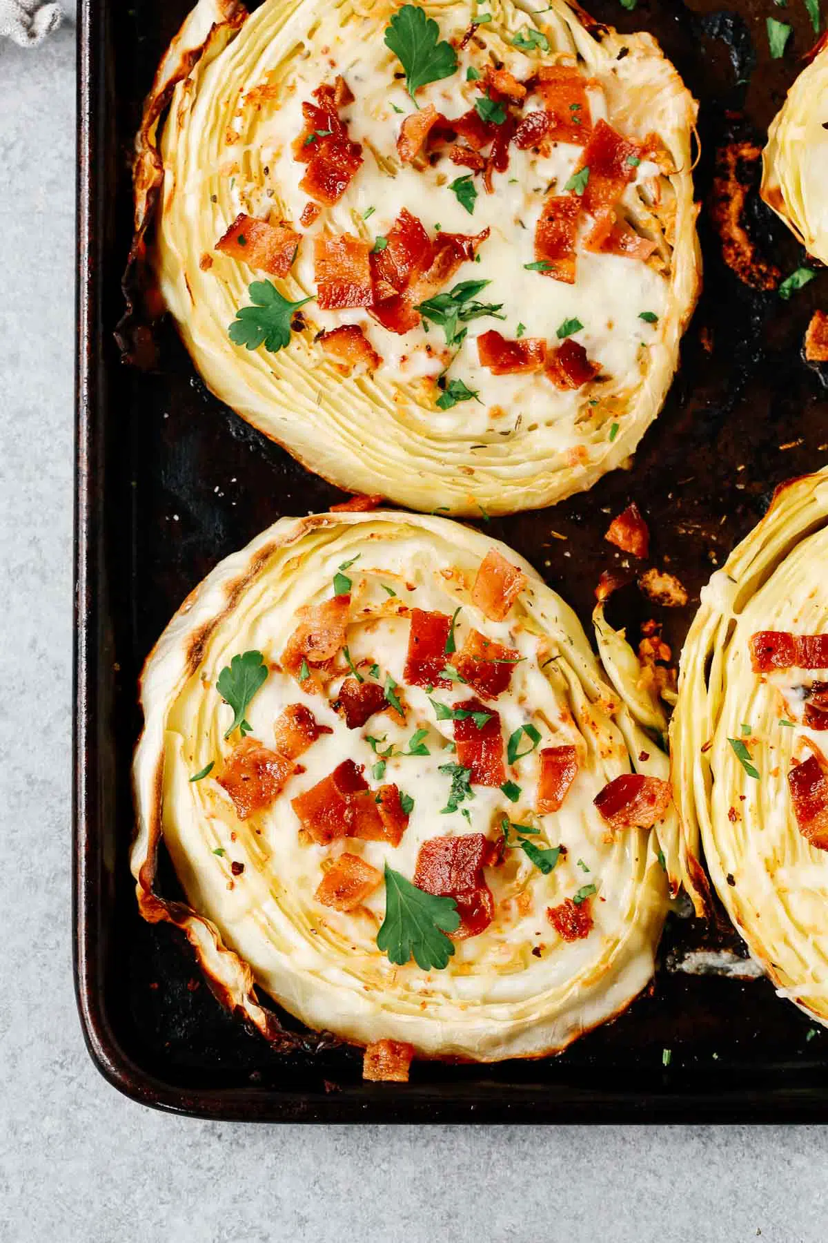 overhead view of roasted cabbage steaks with mozzarella and bacon on a baking sheet