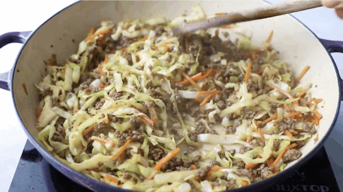 Cooking ground beef in a skillet with a wooden spoon as the first step for making Egg Roll in a Bowl.