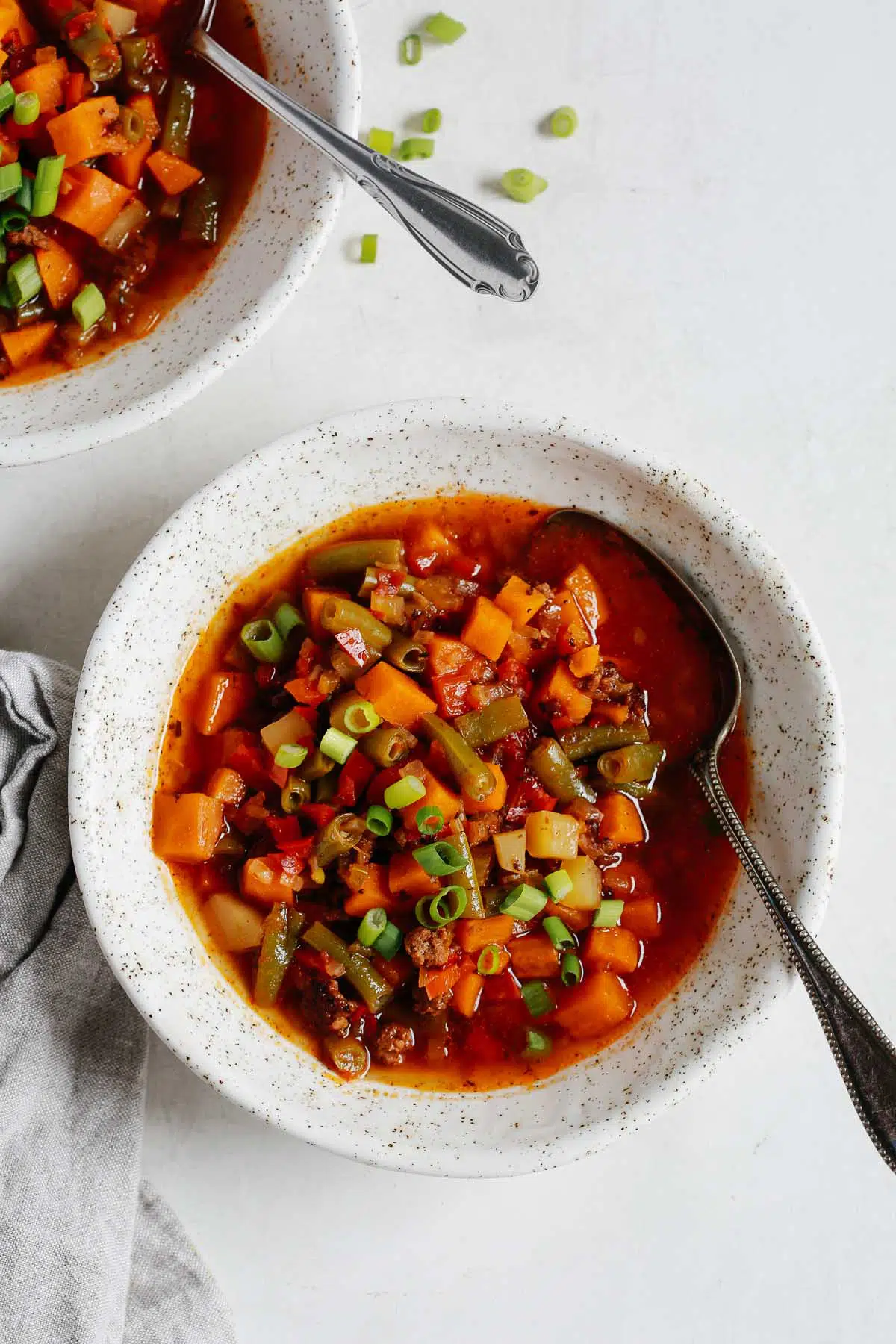 Ground beef vegetable soup in a white bowl with a spoon.