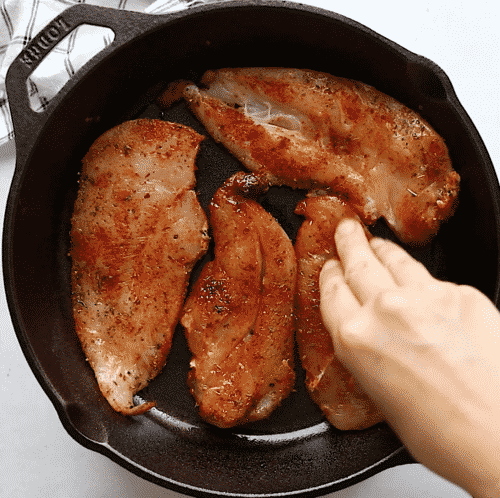 overhead view of a cast iron skillet containing chicken breast and spices